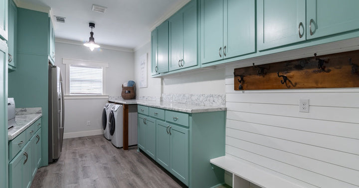 A spacious laundry room with aqua cabinets and white walls features a built-in bench area with hooks.