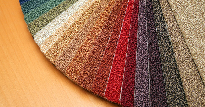 Colorful carpet swatches sit on a laminate surface, transitioning from light blue tones to beige from left to right.